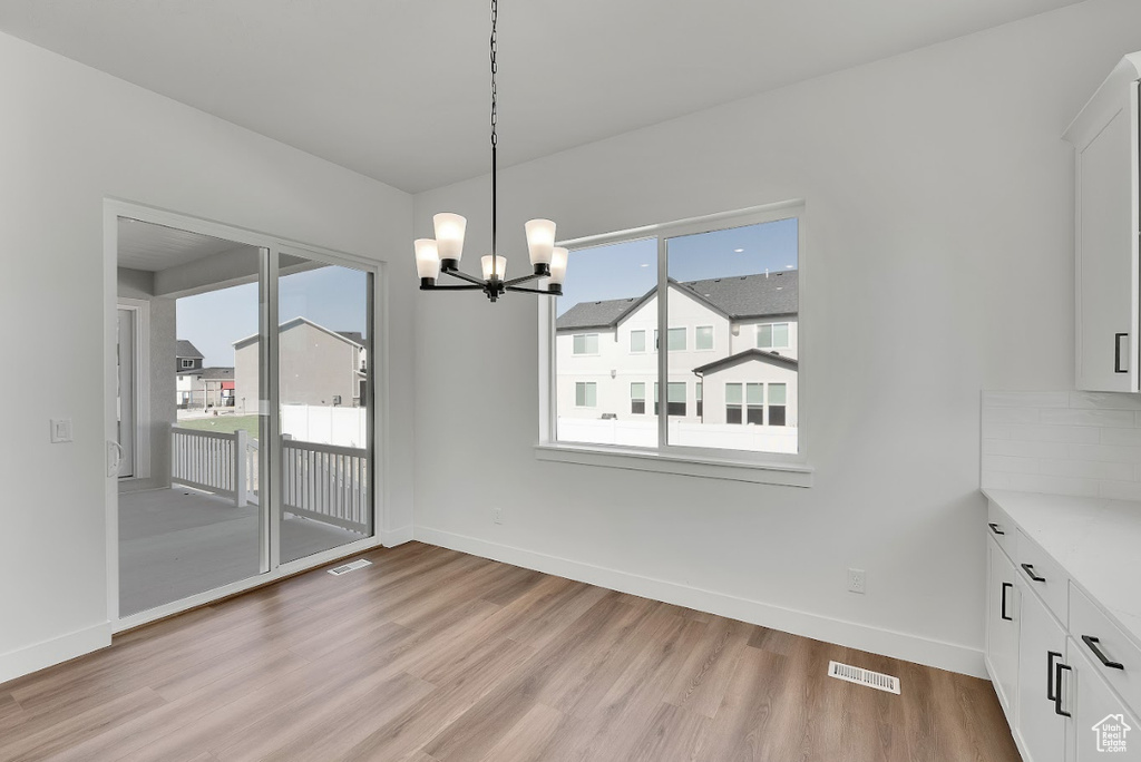 Unfurnished dining area featuring light wood-type flooring, a chandelier, and plenty of natural light