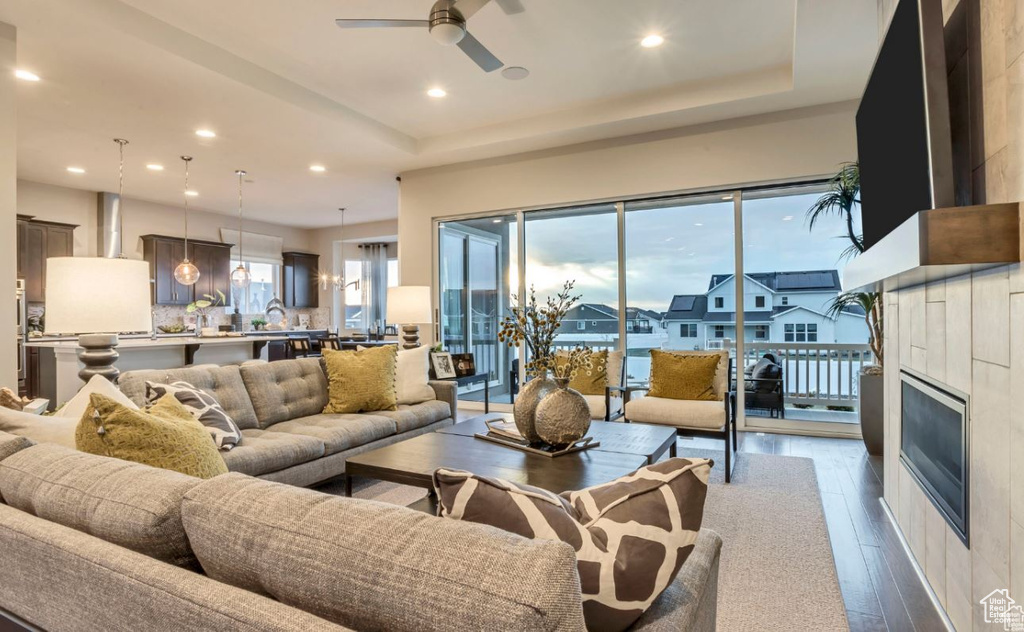 Living room featuring hardwood / wood-style flooring, a tile fireplace, a raised ceiling, and ceiling fan