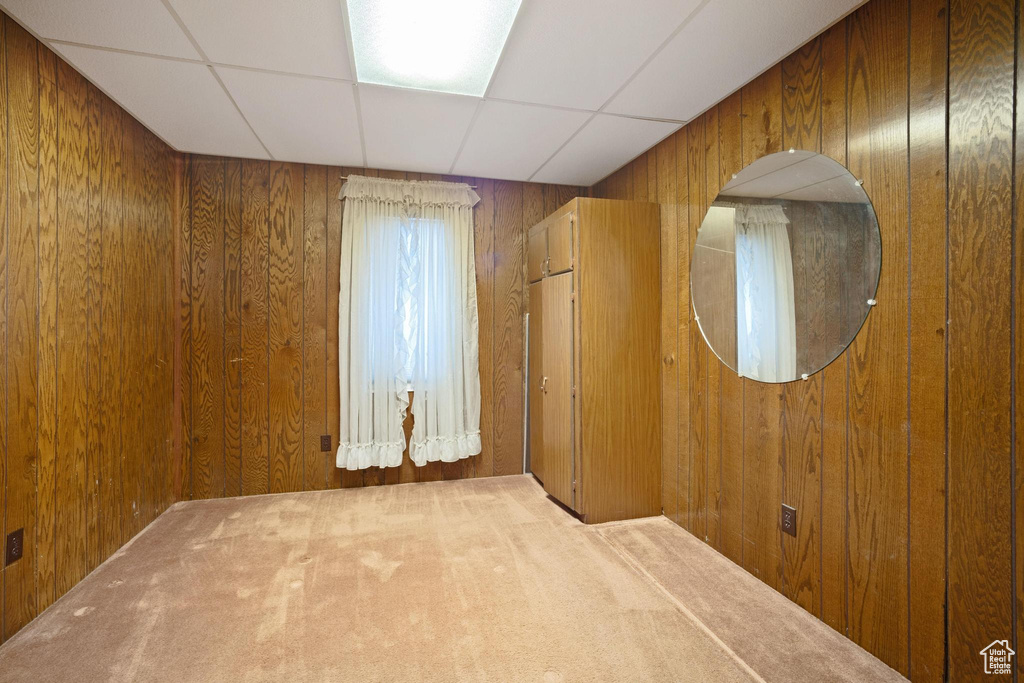 Empty room featuring a paneled ceiling, wooden walls, and carpet floors