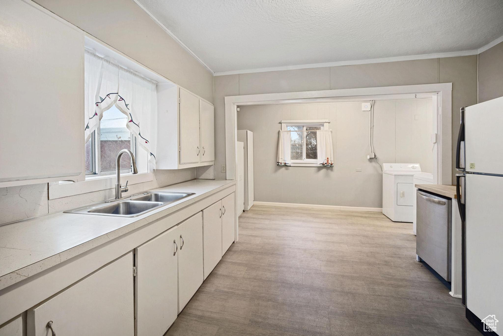 Kitchen featuring washer / dryer, sink, stainless steel dishwasher, white fridge, and white cabinets