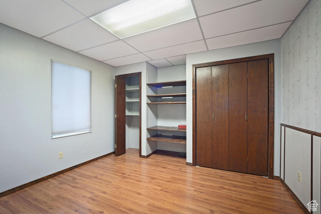 Unfurnished bedroom with a drop ceiling, light hardwood / wood-style floors, and multiple closets