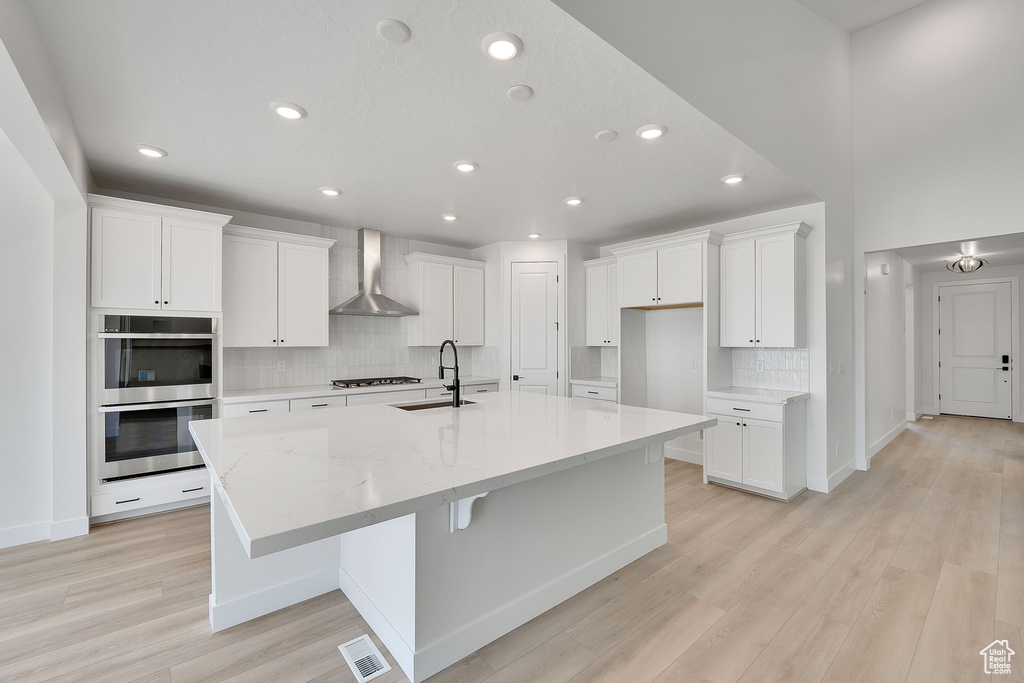 Kitchen featuring wall chimney exhaust hood, a sink, stainless steel double oven, tasteful backsplash, and a large island