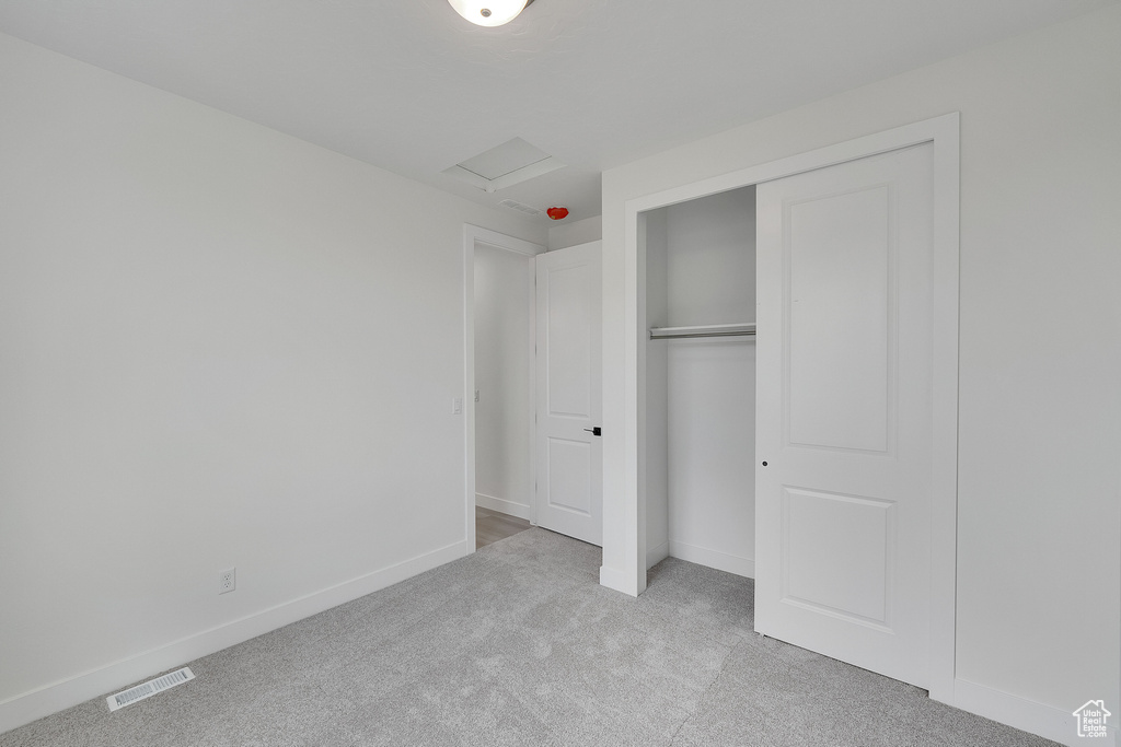 Unfurnished bedroom featuring light colored carpet, attic access, baseboards, and a closet