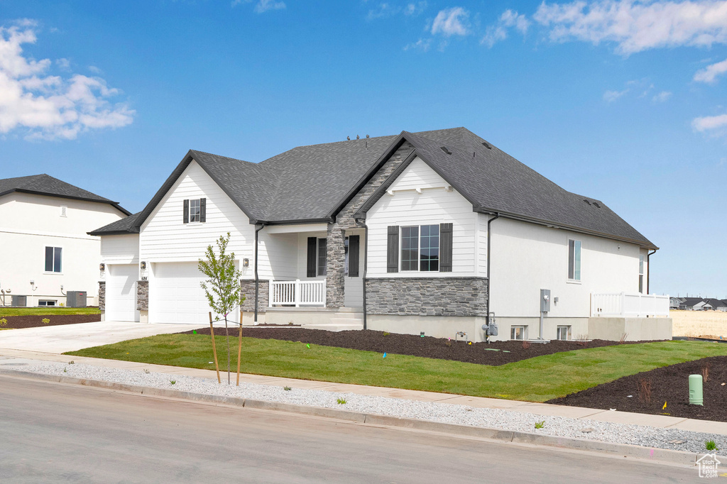 View of front of house with stone siding, driveway, a front yard, an attached garage, and a shingled roof