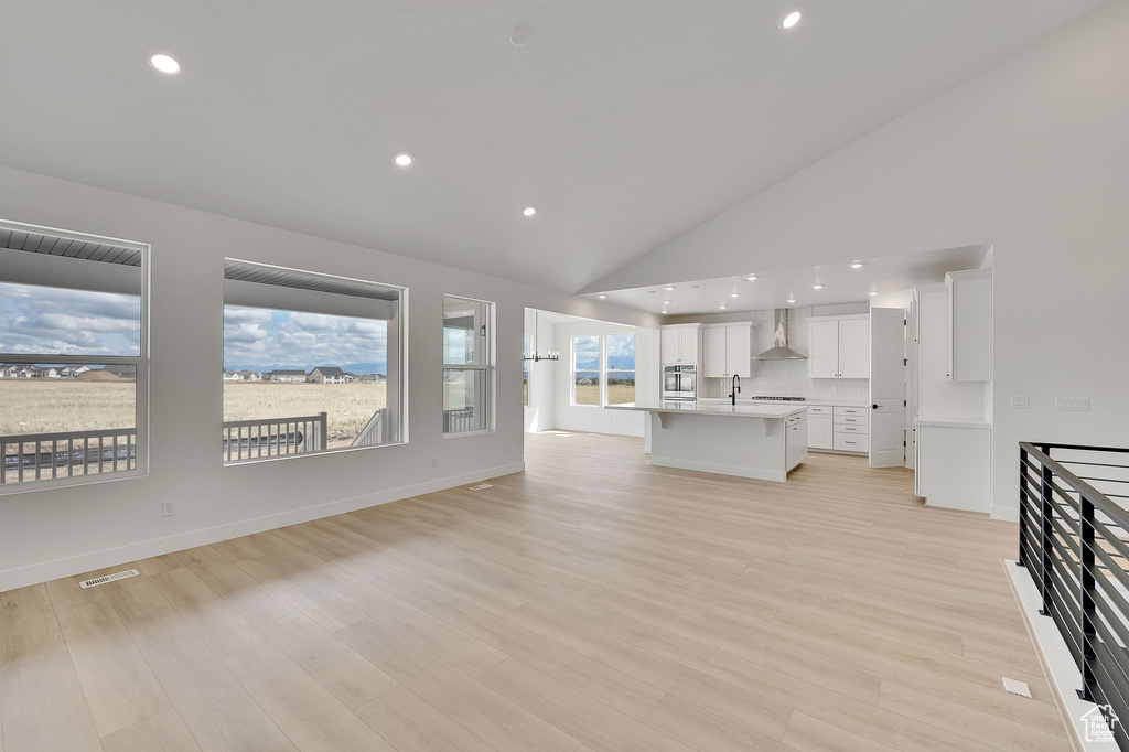 Unfurnished living room with a sink, recessed lighting, light wood-style floors, baseboards, and high vaulted ceiling