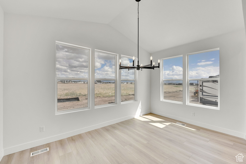 Unfurnished dining area with vaulted ceiling, a chandelier, wood finished floors, and baseboards