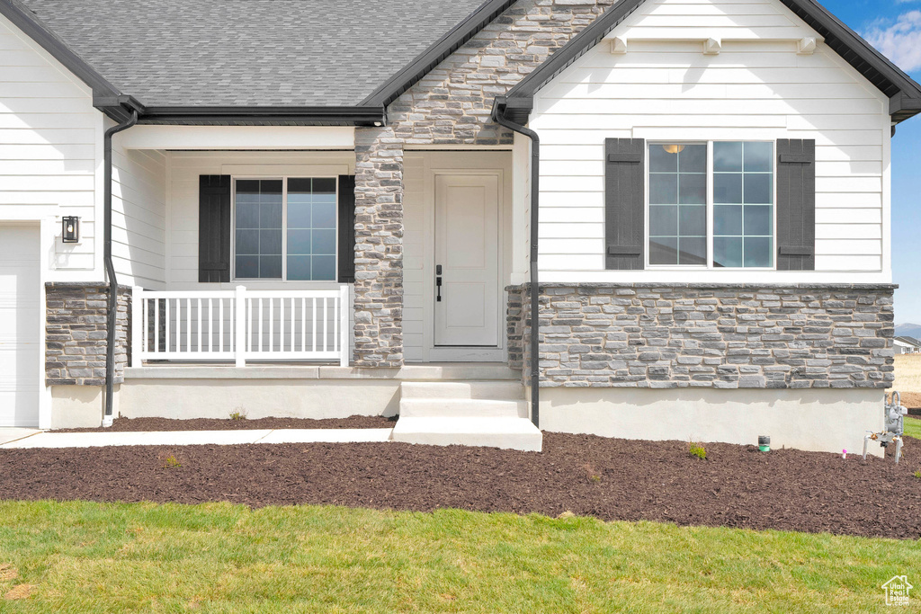 Entrance to property featuring stone siding, roof with shingles, a garage, and covered porch