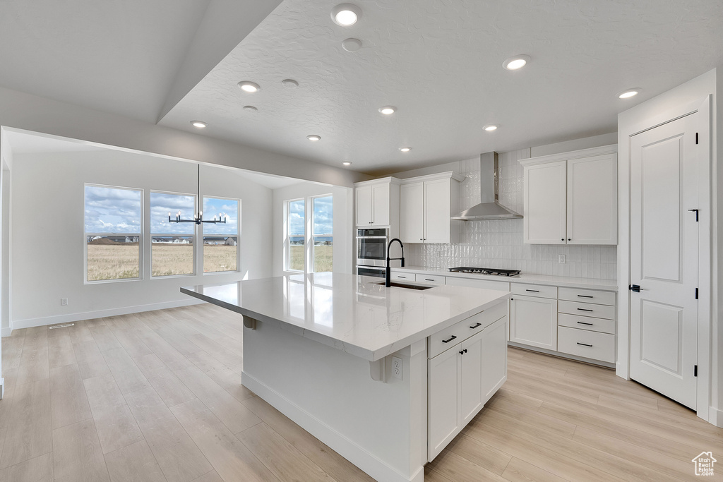 Kitchen with wall chimney range hood, a sink, stainless steel oven, gas cooktop, and recessed lighting