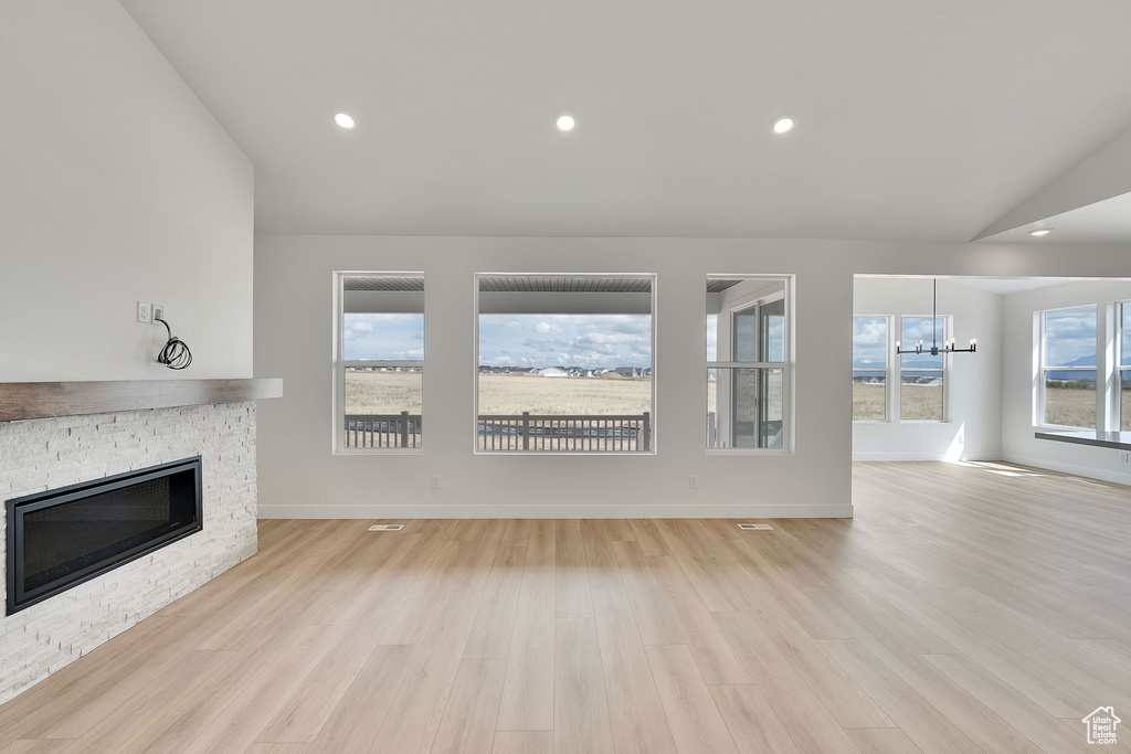Unfurnished living room featuring a stone fireplace, a chandelier, light wood-type flooring, baseboards, and recessed lighting