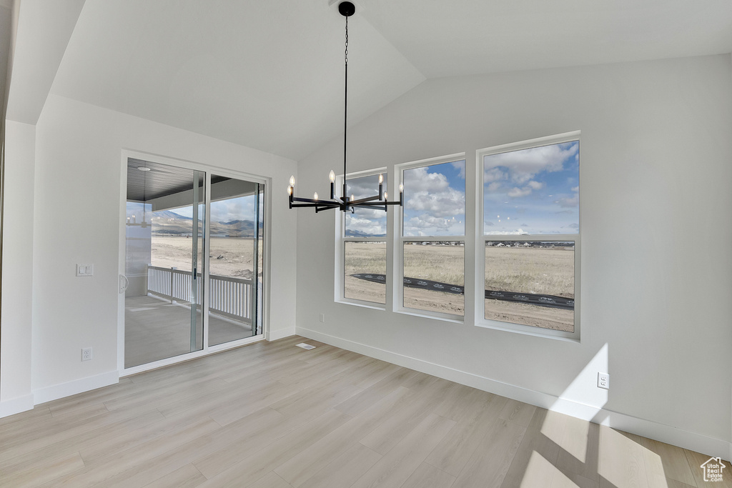 Unfurnished dining area featuring a chandelier, wood finished floors, lofted ceiling, and baseboards