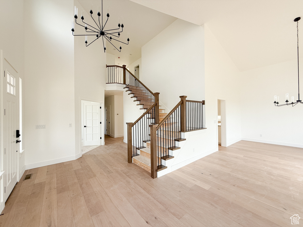 Foyer with a chandelier, high vaulted ceiling, stairway, and light wood-style floors