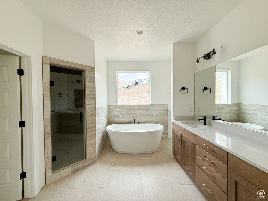 Full bathroom featuring a stall shower, a soaking tub, tile walls, double vanity, and wainscoting