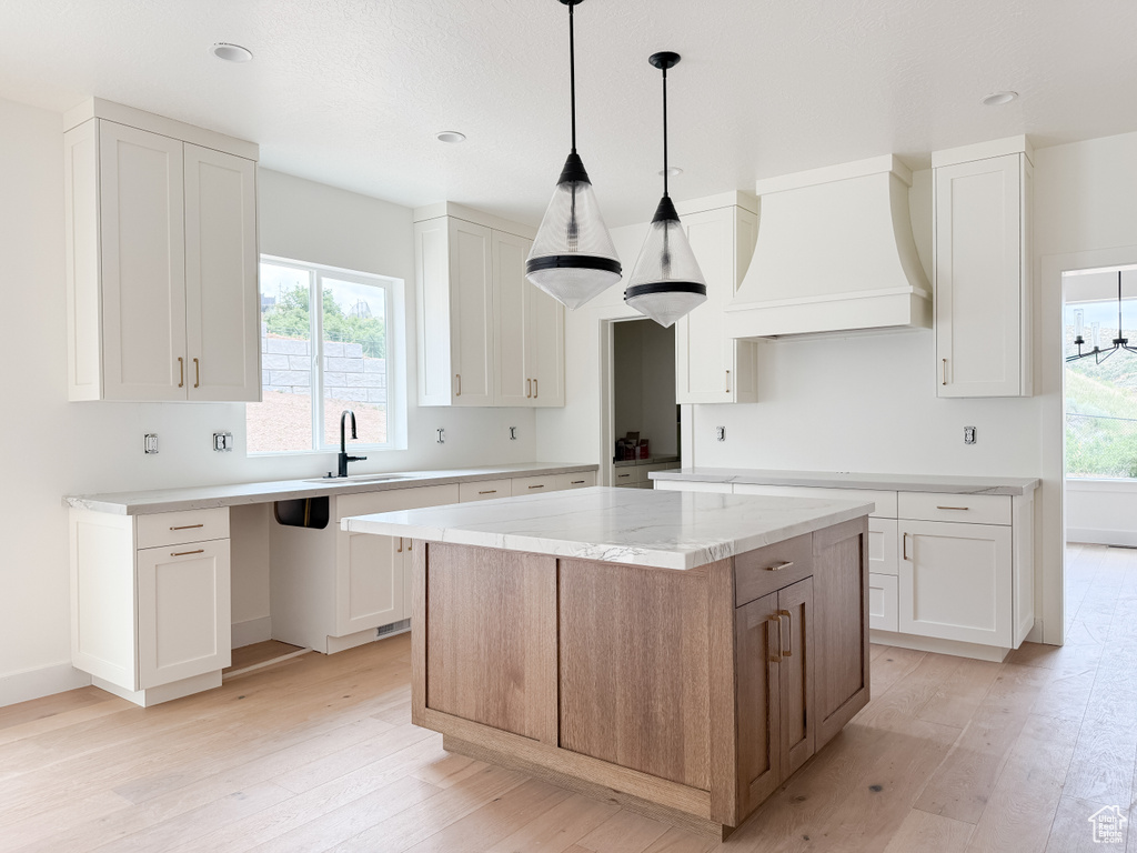 Kitchen with custom exhaust hood, light wood-style floors, white cabinets, and recessed lighting