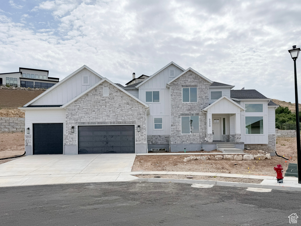 View of front facade featuring board and batten siding, an attached garage, stone siding, and driveway