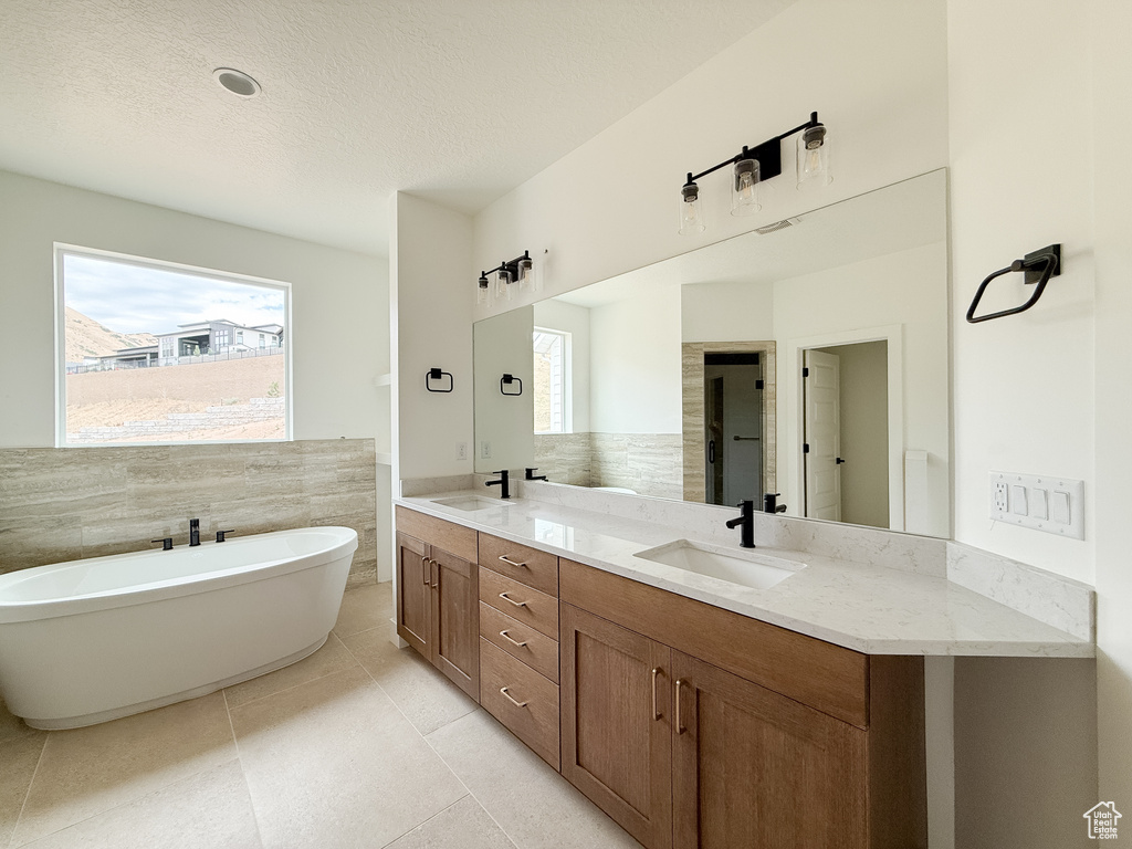Full bathroom featuring double vanity, a freestanding bath, tile patterned floors, a textured ceiling, and tile walls