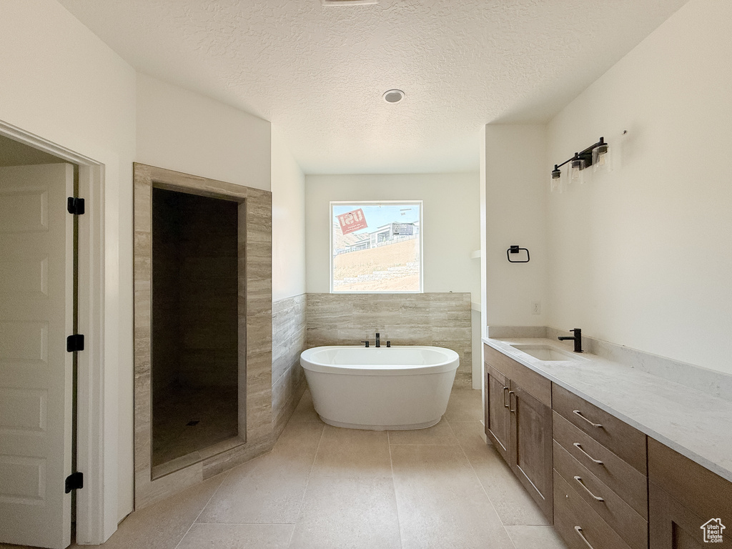 Bathroom with a soaking tub, vanity, tile patterned flooring, and a textured ceiling