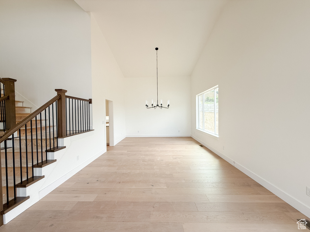 Unfurnished dining area featuring high vaulted ceiling, a chandelier, light wood-style flooring, and stairs