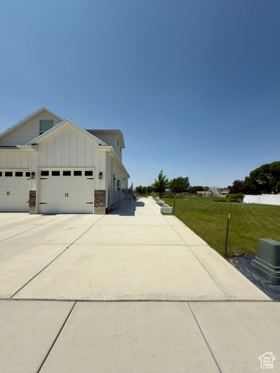 View of property exterior featuring board and batten siding, driveway, an attached garage, and a lawn
