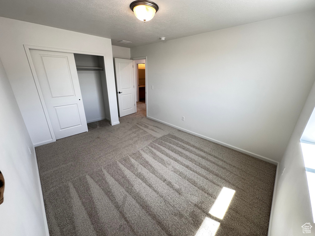 Unfurnished bedroom featuring a closet, carpet floors, baseboards, and a textured ceiling