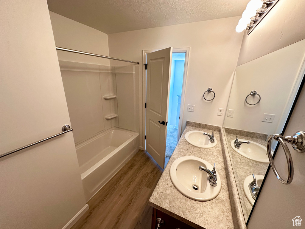 Full bath with wood finished floors, double vanity, a textured ceiling, and  shower combination