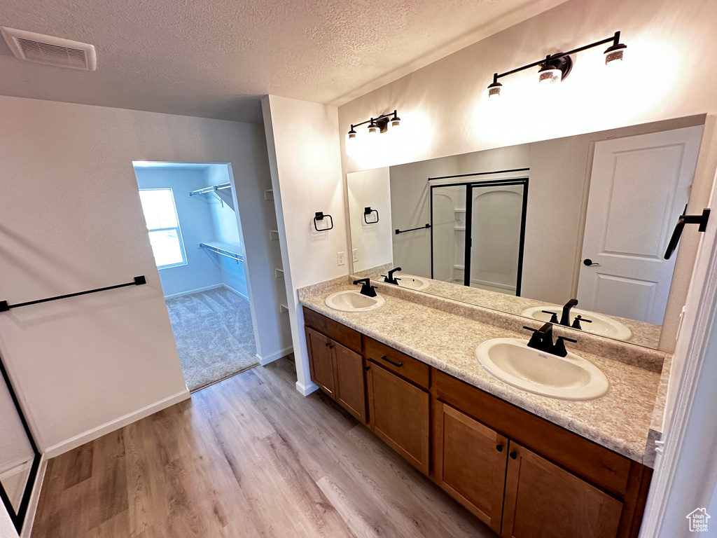 Bathroom featuring a textured ceiling, wood finished floors, double vanity, and a shower