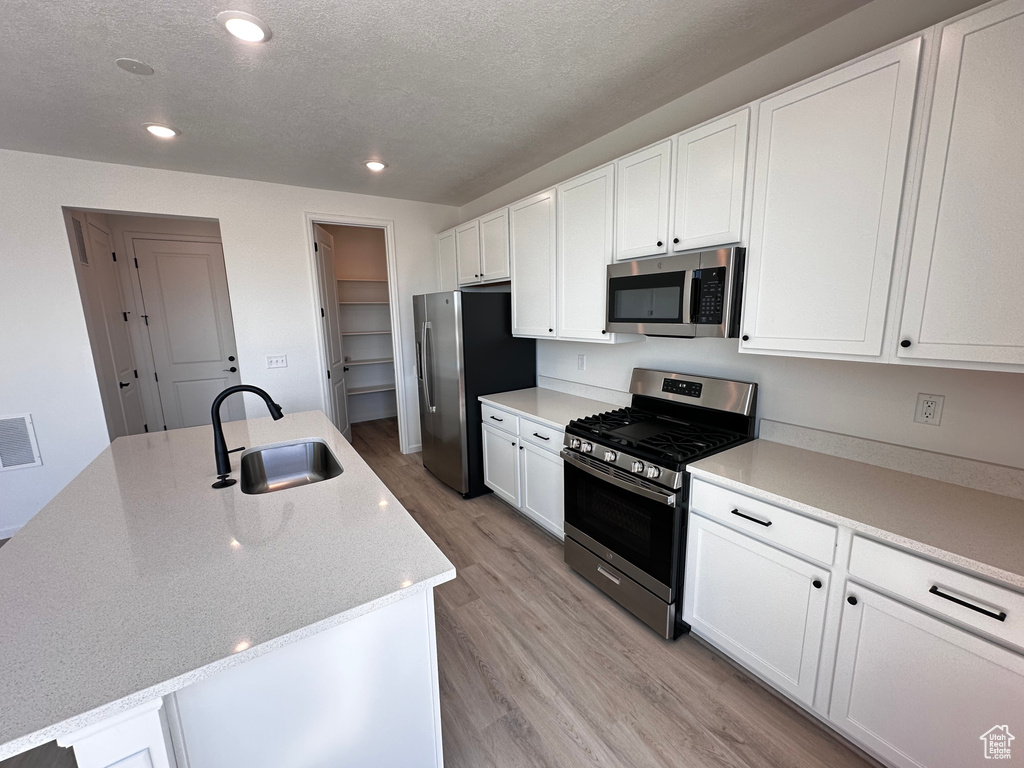 Kitchen featuring appliances with stainless steel finishes, a sink, light wood finished floors, white cabinetry, and recessed lighting