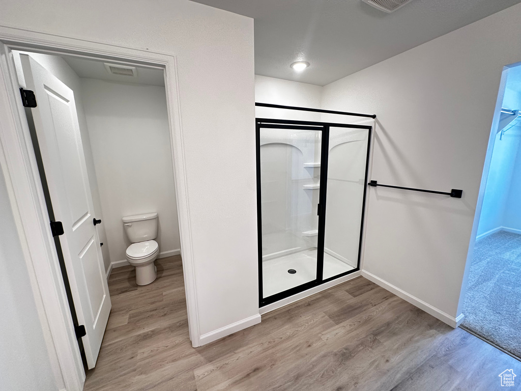 Full bath with a shower stall, wood finished floors, baseboards, and toilet