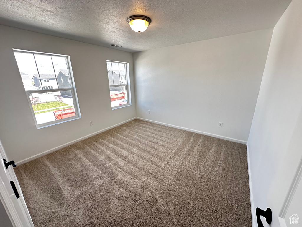Empty room featuring a textured ceiling, carpet flooring, and baseboards