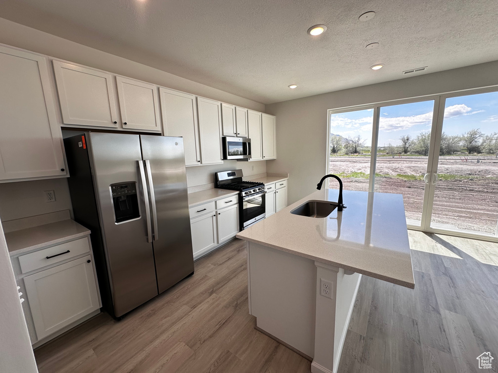 Kitchen with appliances with stainless steel finishes, a sink, a textured ceiling, white cabinetry, and light wood-type flooring