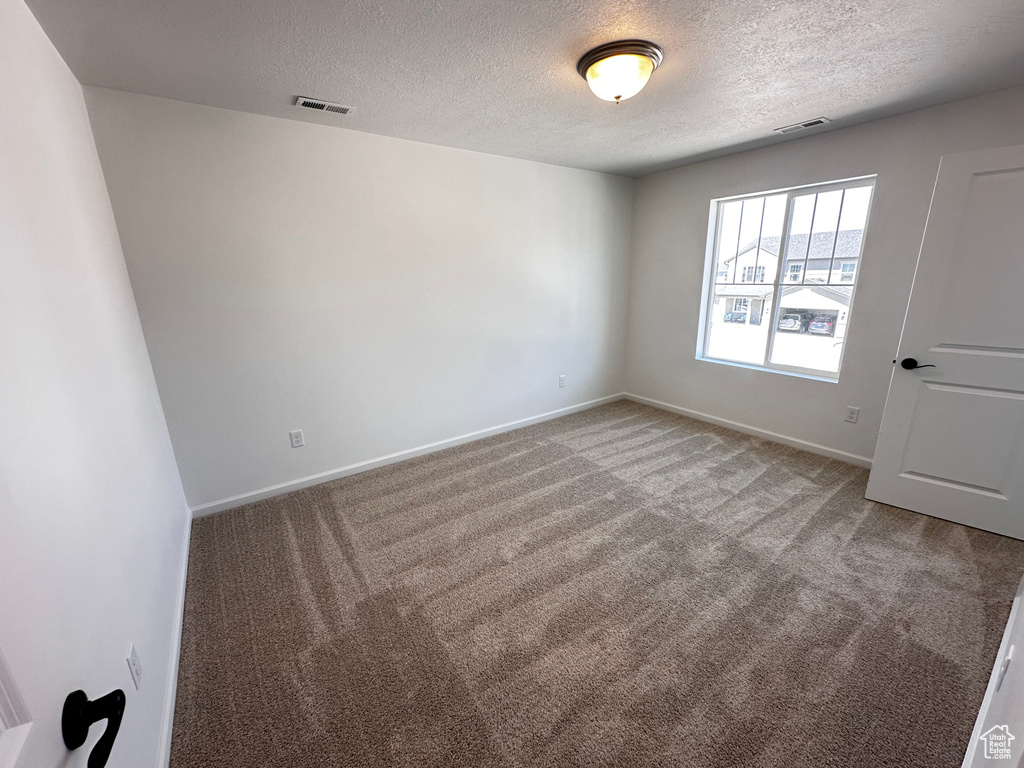 Empty room featuring carpet, a textured ceiling, and baseboards