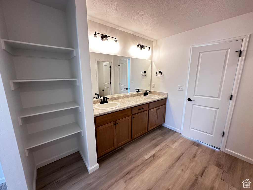 Full bath with wood finished floors, a textured ceiling, double vanity, and baseboards