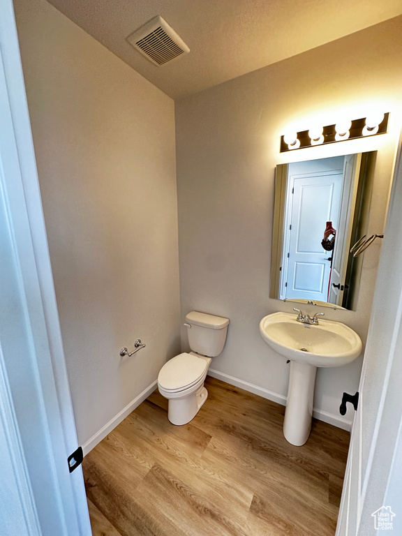 Half bath with toilet, wood finished floors, baseboards, and a sink