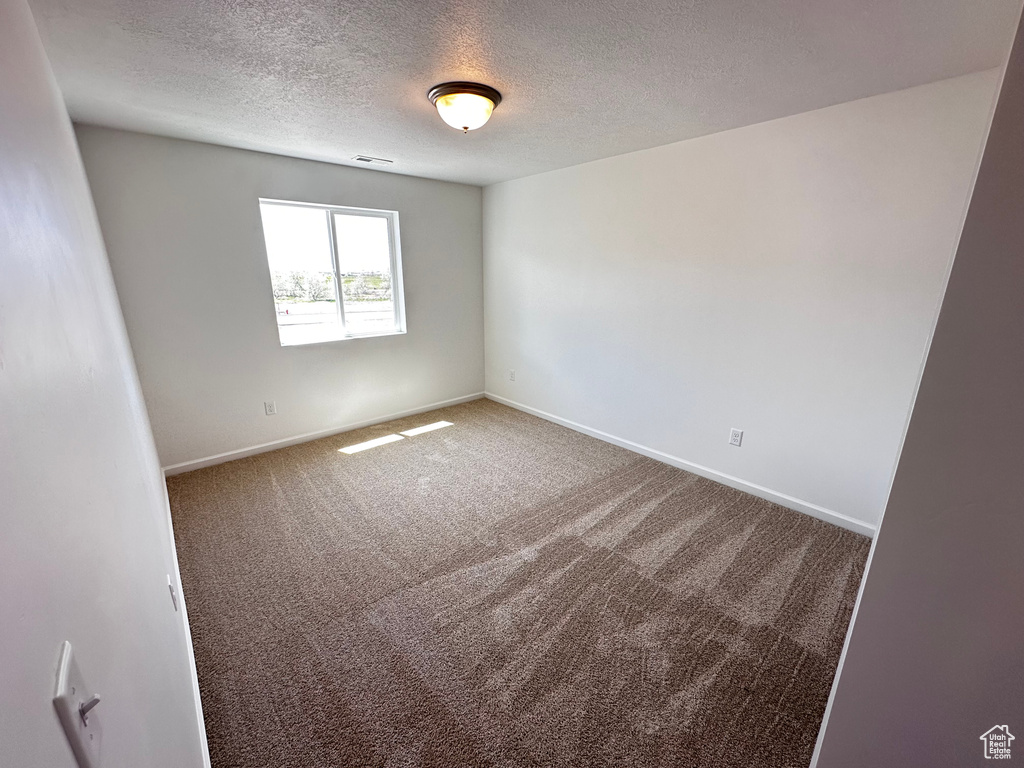 Carpeted empty room with a textured ceiling and baseboards