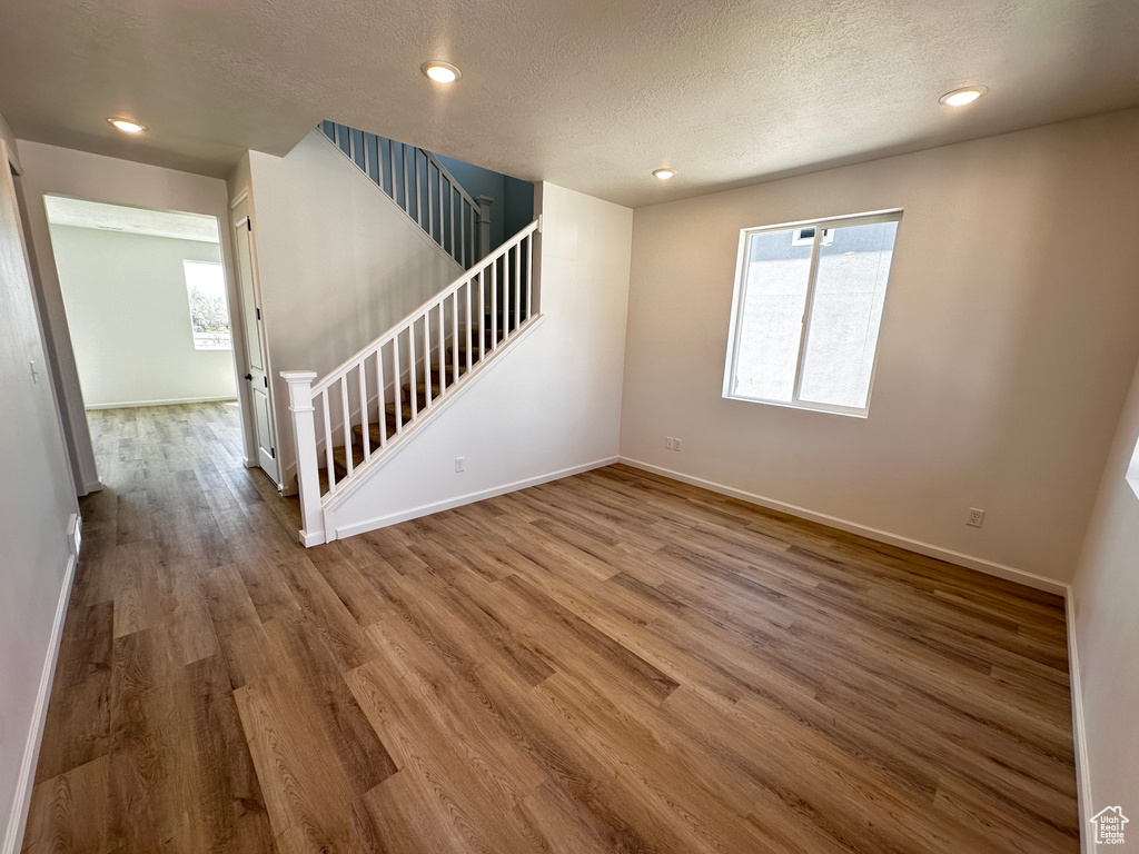 Unfurnished living room featuring wood finished floors, baseboards, stairway, recessed lighting, and a textured ceiling