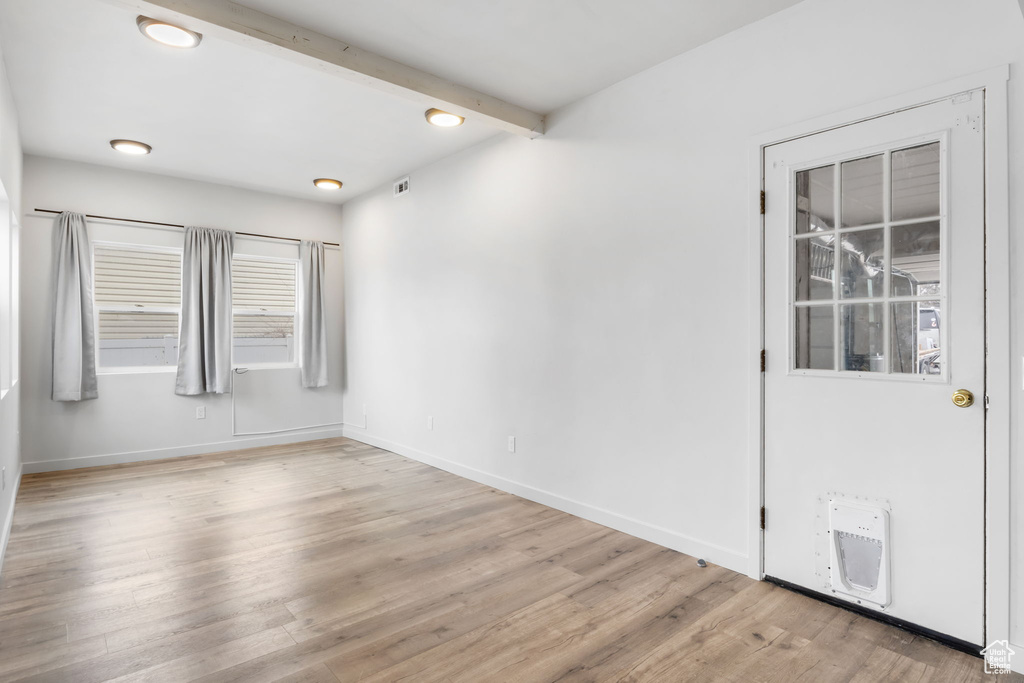 Empty room featuring beamed ceiling and light hardwood / wood-style floors