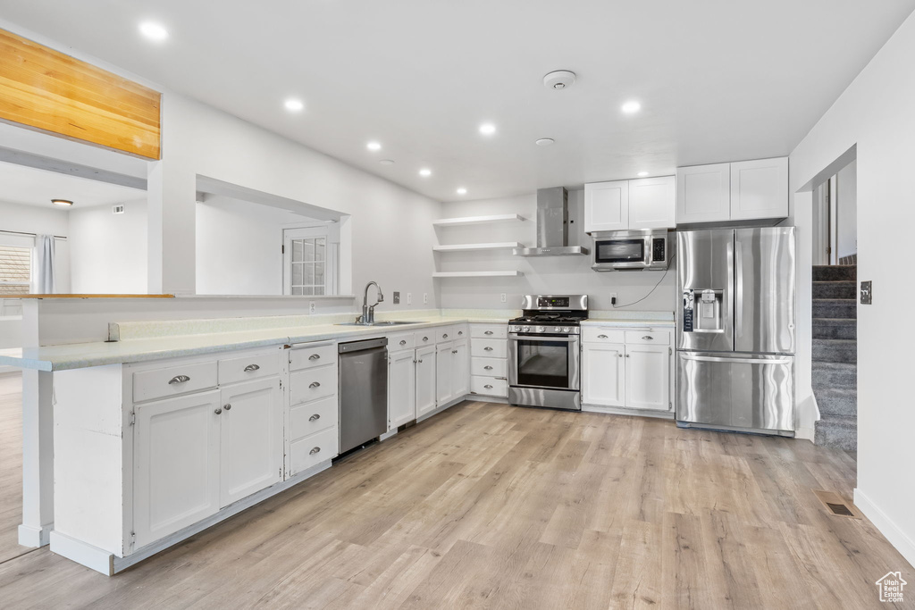 Kitchen featuring white cabinetry, wall chimney range hood, stainless steel appliances, and sink