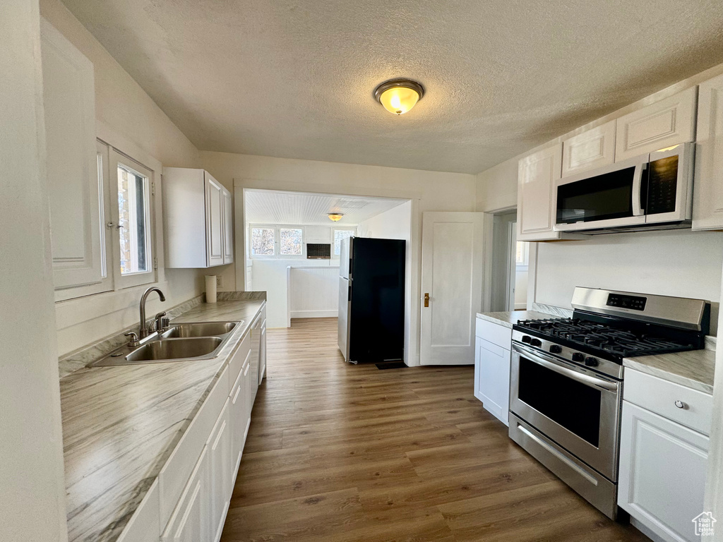 Kitchen featuring dark wood-style flooring, white cabinets, stainless steel appliances, and a sink