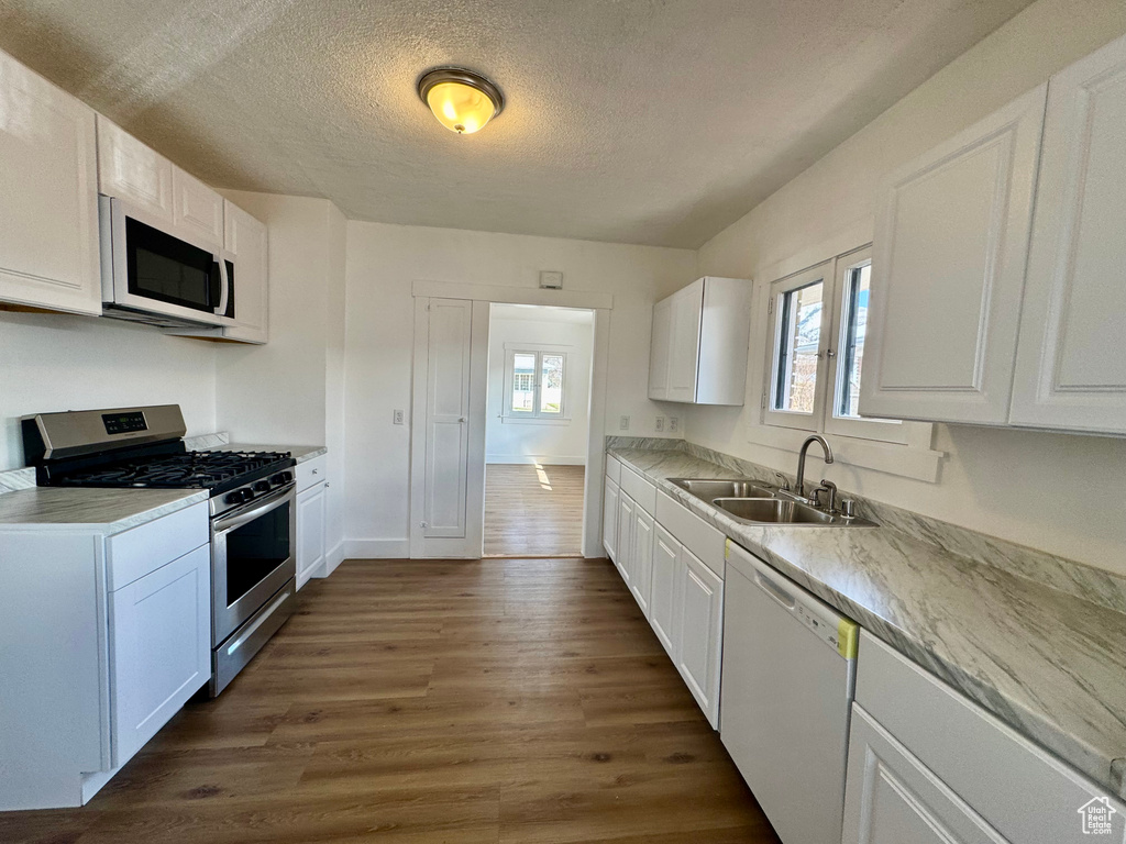 Kitchen featuring dark wood finished floors, a textured ceiling, white appliances, white cabinetry, and a sink