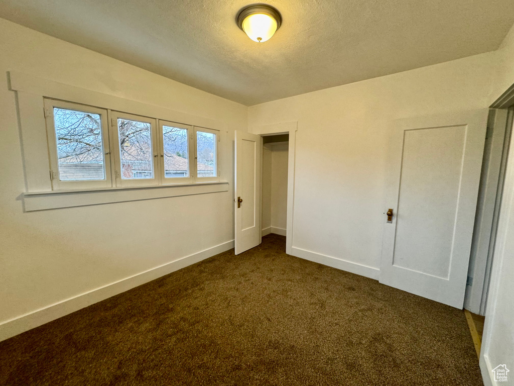 Unfurnished bedroom featuring a textured ceiling and dark colored carpet