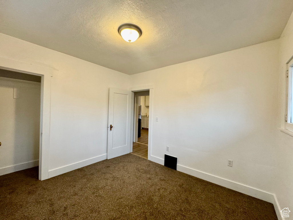 Unfurnished bedroom with dark carpet and a textured ceiling