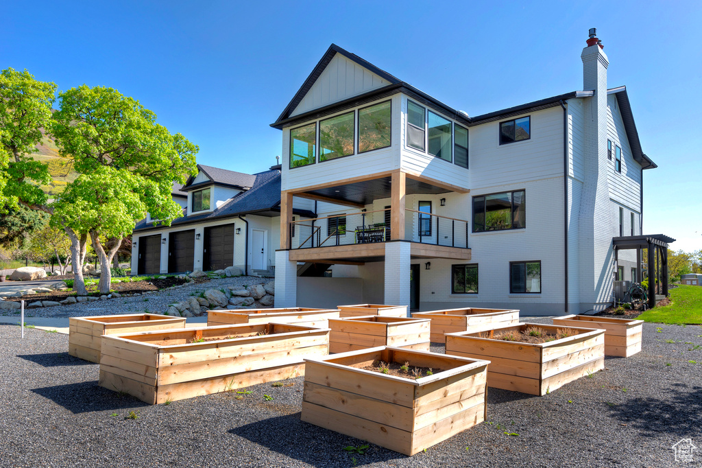 Rear view of property featuring board and batten siding, a chimney, a balcony, and a vegetable garden