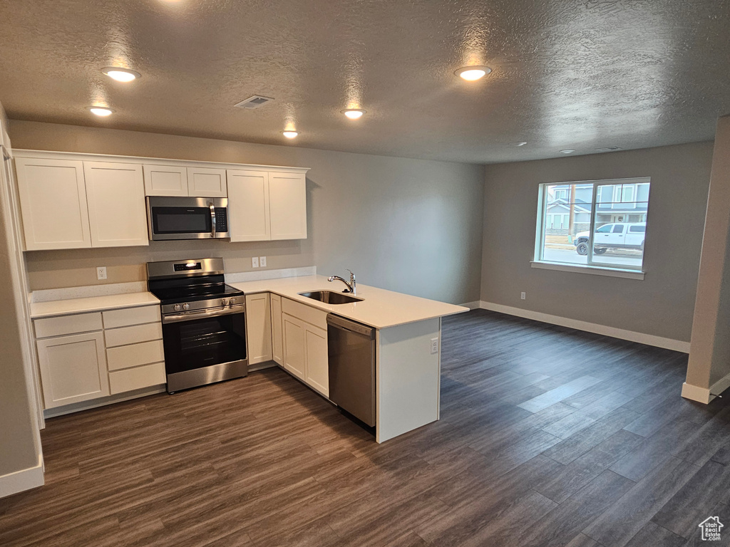 Kitchen with sink, dark wood-type flooring, appliances with stainless steel finishes, white cabinets, and kitchen peninsula