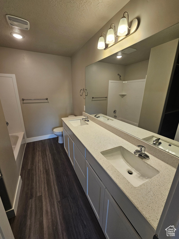 Full bathroom featuring hardwood / wood-style flooring,  shower combination, vanity, a textured ceiling, and toilet