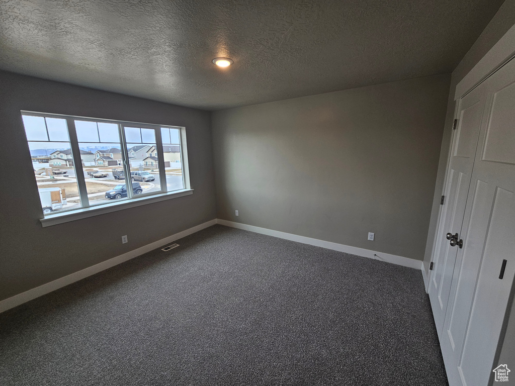 Spare room with a textured ceiling and dark colored carpet