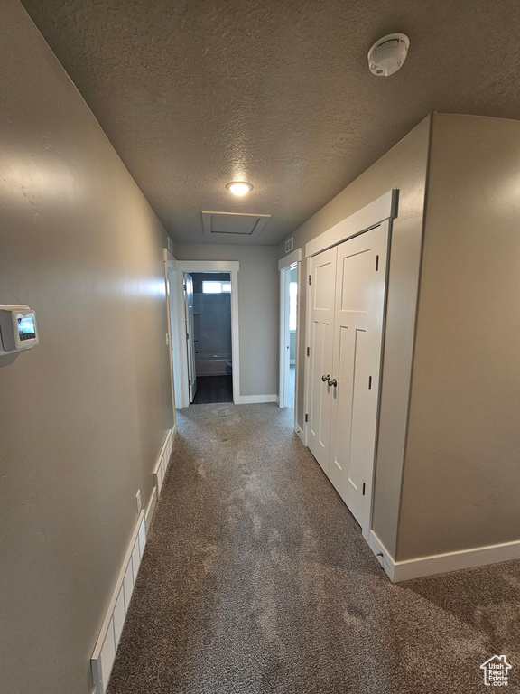 Hall featuring dark carpet and a textured ceiling