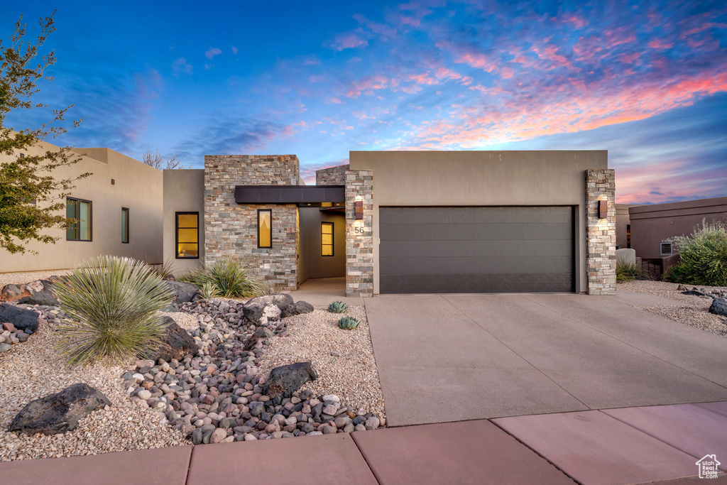 View of front of property featuring a garage, concrete driveway, stone siding, and stucco siding