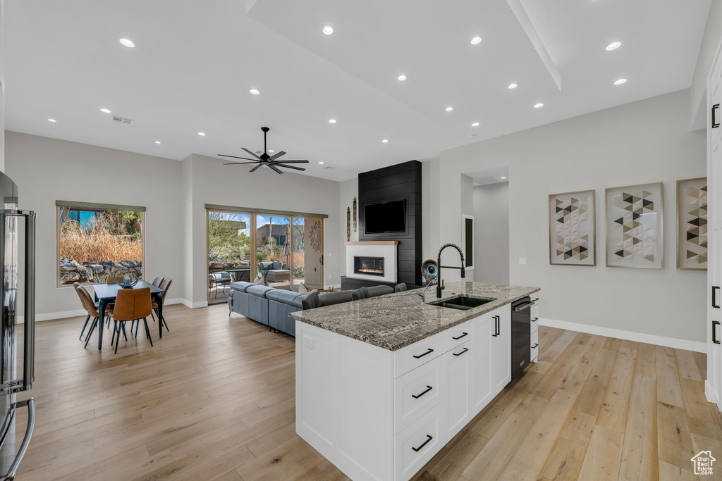 Kitchen with sink, stone countertops, a large fireplace, a kitchen island with sink, and white cabinets