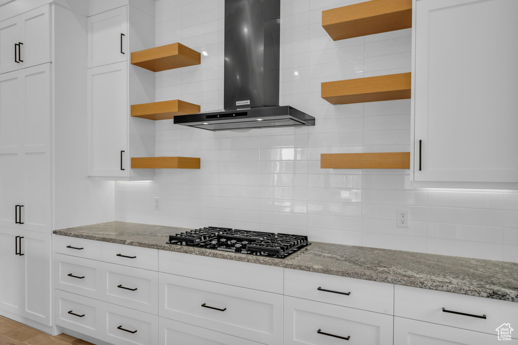 Kitchen with white cabinetry, light stone countertops, wall chimney range hood, and black gas stovetop