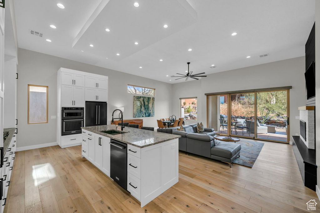 Kitchen featuring sink, white cabinets, a kitchen island with sink, black appliances, and light stone countertops