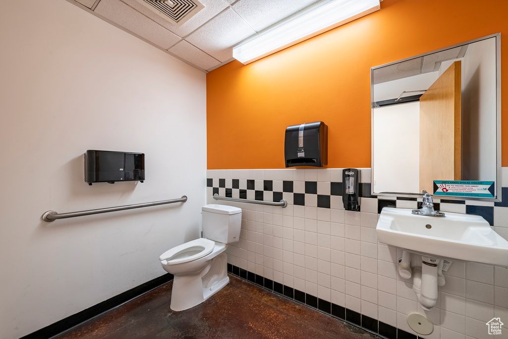 Bathroom with concrete flooring, sink, tile walls, toilet, and a drop ceiling